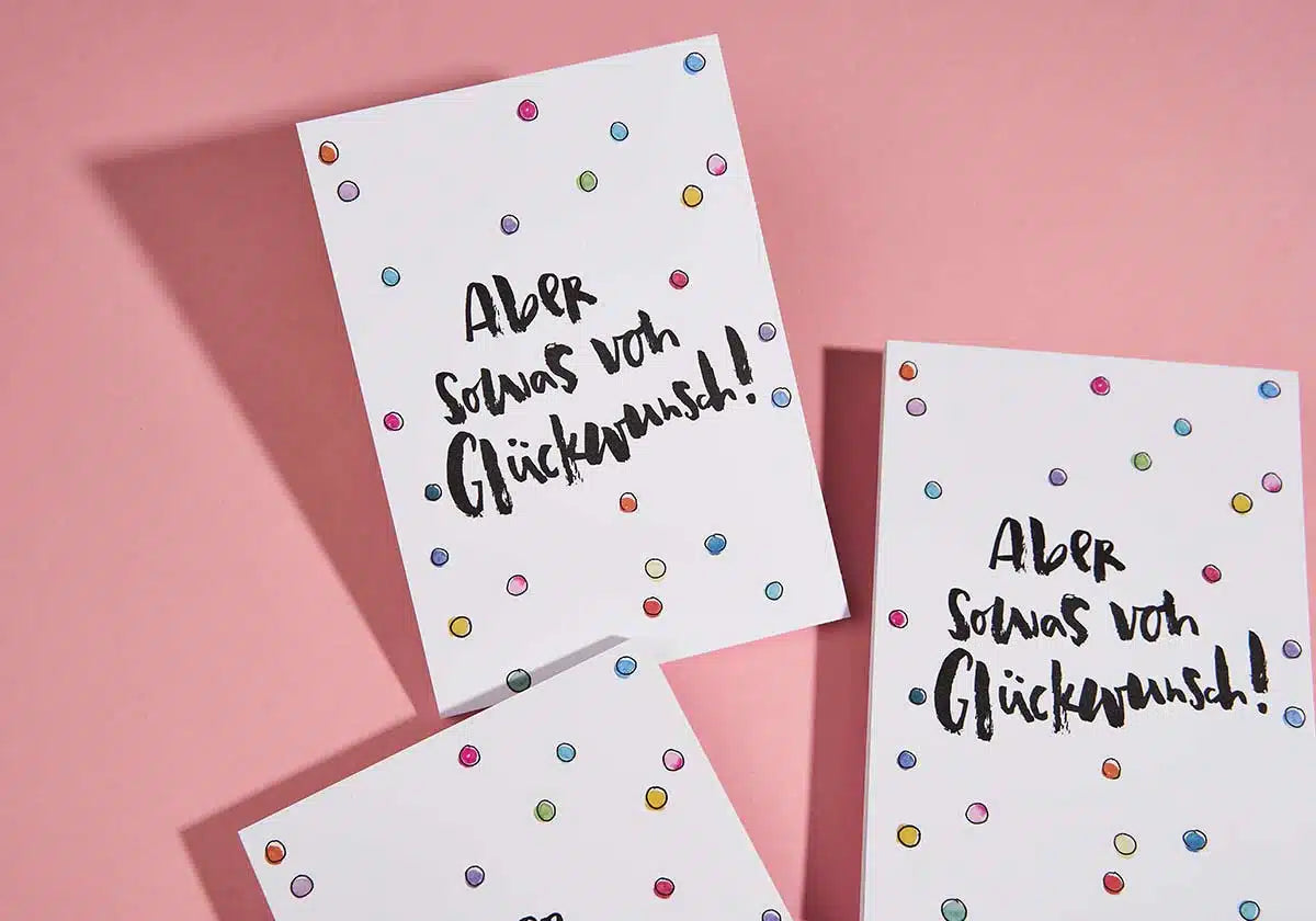 Drei Grußkarten auf rosa Hintergrund, jeweils verziert mit bunten Punkten und dem deutschen Text „Aber sowas von Glückwunsch!“ – die perfekte Postkarte „Aber sowas von Glückwunsch“ vonbrushmeetspaper x amoedo für das Teilen freudiger Momente mit herzlichen Glückwünschen.